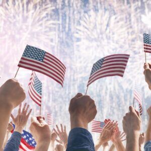 Hands wave American flags during a fireworks show.